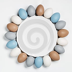 Painted Easter eggs pastel colors beige, gray, blue around white empty plate. Happy Easter holiday card, celebration