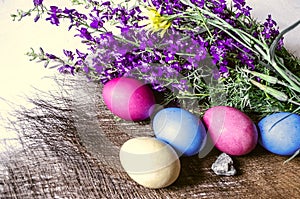 Painted Easter eggs withr the bouquet of purple wild flowers on straw mat