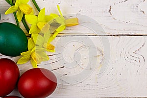 Painted Easter eggs and yellow daffodils on white wooden background. Easter composition. Top view, copy space