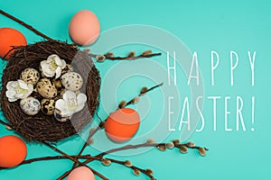 Painted eggs and quail eggs in a nest with willow branches on a turquoise background