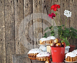 Painted eggs in a red bucket with Easter cakes on a wooden background with homemade pelargonium flowers