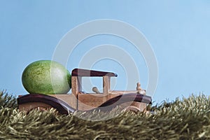 Painted green egg on toy wooden car among grass