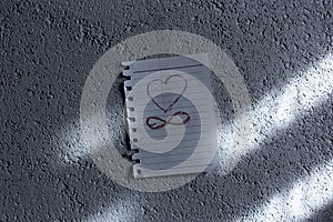 Painted heart and infinity symbol on paper, attached on white textured wall.