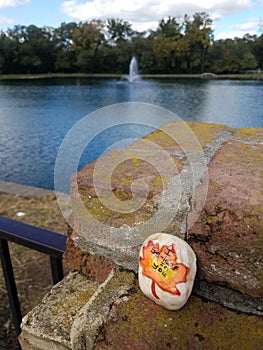 Painted kindness rock by a park lake waiting to spread joy when found