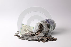 A painted mason jar tipped on its side spilling out coins with a list of bills