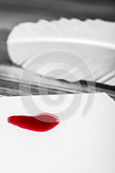 Painted red heart on a white card with a bird feather in the background