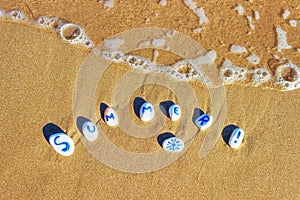 Painted sea pebbles on a summer beach in the oncoming wave.