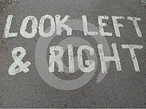 A painted sign on a concrete foot path telling people to look left and right