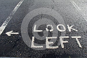 Painted sign on roadway,advising one to look left before crossing