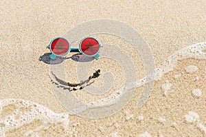 A painted smile on the beach and sunglasses with the flag of Morocco.