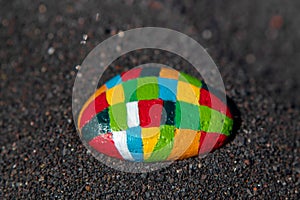 Painted stone with many colors in the black sand of the beach