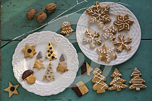 Painted traditional Christmas gingerbreads and custard cookies on white plates on old vintage painted table, various xmas shapes