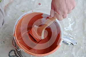 Painter Applies Orange Paint to Brush from Pail photo
