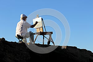 A painter artist is painting a picture of a sea landscape above a rock in a place of the coast of Alicante in Spain