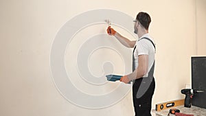 Painter in black overalls painting white wall using roller