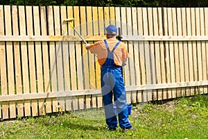 Painter in blue dungarees decorating wooden fence
