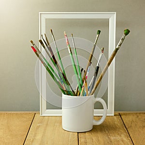 Painter brushes in white cup on wooden table. Cup for logo display mock up