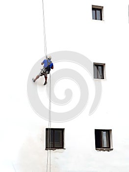 Painter of building facades. Vertical works. Worker hanging on a rope to paint white wall with roller. The vertical worker is