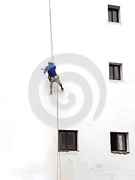 Painter of building facades. Vertical works. Worker hanging on a rope to paint white wall with roller. The vertical worker is