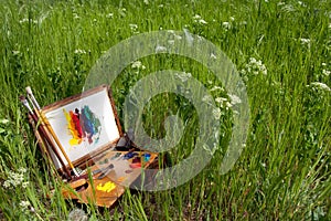 Painter case on grass with palette and artistic tools