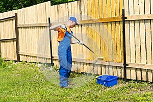 Painter decorates wooden fence with yellow paint