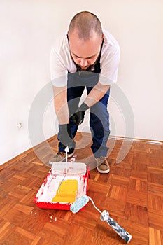 Painter holds roller brush paint in hand and mixes yellow paint in container and red bowl for color mixing.