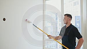 Painter man. A bearded construction worker in a blue overalls is painting a wall in the hallway. He uses a roller. Man