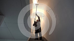 Painter man painting ceiling of staircase with roller tool