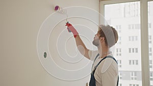 Painter man painting the wall in home, with paint roller and white color paint. Close up of male in gloves holding