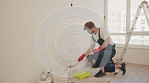 Painter man painting the wall in home, with paint roller and white color paint. Close up of male in gloves holding