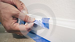 Painter Man Removing masking blue tape from molding, baseboard