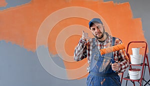 Painter man standing before wall and pointing to the back behind with hand and thumbs up, confident