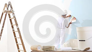 Painter man at work with color swatches samples, wall painting concept, ladder in the background and brushes and bucket in the for