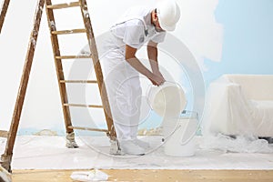 Painter man at work pour into the bucket color for painting the