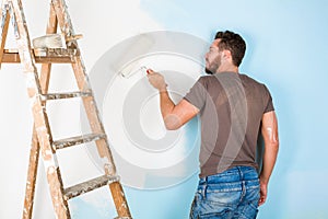 Painter in paint splattered shirt painting a wall