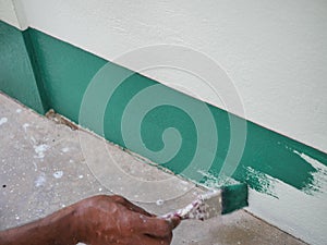 Painter painting green color acrylic on house concrete wall with a paintbrush