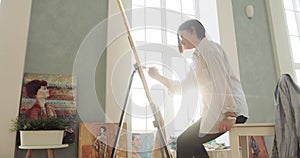 Painter painting modern art picture using brush on canvas sitting near easel.