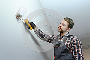 Painter painting a wall with paint roller. Builder worker painting surface with white color