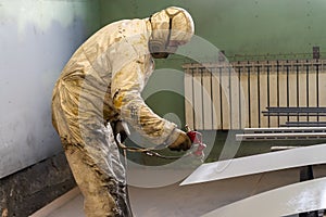 The painter in protective overalls works with a spray gun