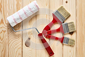 Painter roller and paintbrushes at wooden surface