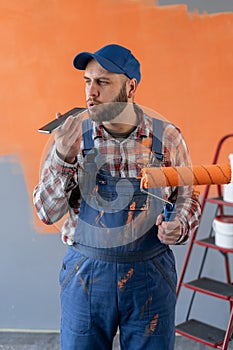 Painter with roller renovates wall. Smartphone aids painter in renovation.
