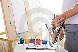 Painter`s hand holds brush on the background of easel