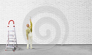 Painter standing on concrete floor and painting white brick wall with paint brush.