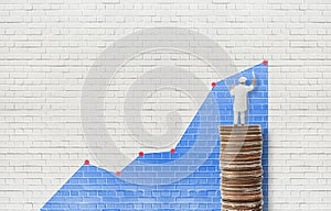 Painter standing on stacked silver coins and painting financial business growth graph on rough concrete wall.