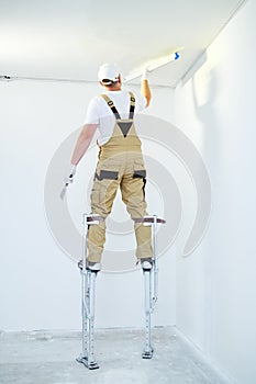 Painter in stilts with putty knife. Plasterer smoothing ceiling surface at home renewal