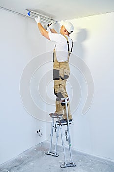 Painter in stilts with putty knife. Plasterer smoothing ceiling surface at home renewal