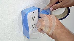 Painter Using Masking Blue Tape to Secure Electric Outlet. Preparation For Room Painting