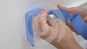 Painter Using Masking Blue Tape to Secure Electric Outlet. Preparation For Room Painting