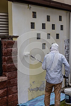 Painter worker adding undercoat foundation paint onto wall with roller at residential building in renovation