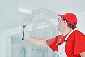 Painter worker with roller painting ceiling surface into white